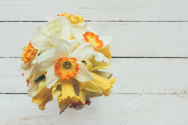 bouquet of fresh flowers of daffodils on a white wooden background with space for text, top view
