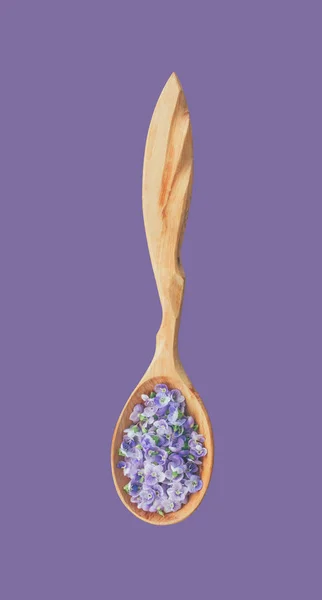 Delikatny kwiat niebieski płatki w zbliżeniu drewnianą łyżką na białym tle na fioletowym tle, widok z góry — Zdjęcie stockowe