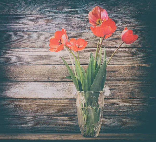 Bouquet of flowers red tulips in a glass vase on a wooden background barn boards closeup. retro tinted photo — Stock Photo, Image