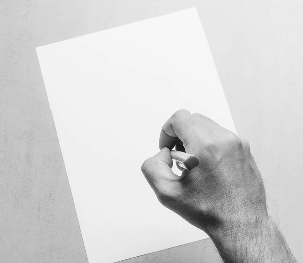 Männerhand mit Kugelschreiber und leerem weißen Blatt Papier auf grauem Hintergrund, Nahaufnahme von oben. Schwarz-Weiß-Fotomock für Text, Glückwünsche, Phrasen, Schriftzüge — Stockfoto