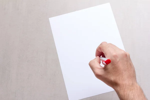 Mans mão com uma caneta esferográfica e branco em branco folha de papel sobre um fundo cinza, vista superior close-up. mock up para texto, parabéns, frases, letras — Fotografia de Stock