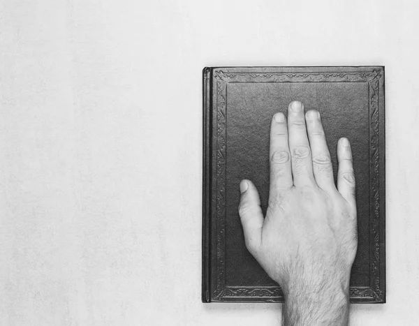 Mão do homem sobre o livro, o juramento sobre a Bíblia. vista superior close-up. foto em preto e branco. mock up para texto, frases, letras — Fotografia de Stock