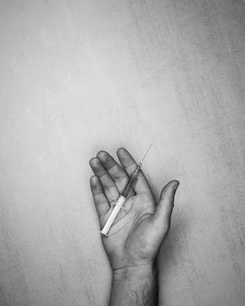 Jeringa médica con aguja y medicamentos en una palma abierta masculina sobre un fondo gris, vista superior. foto en blanco y negro. maqueta para texto, frases, letras — Foto de Stock