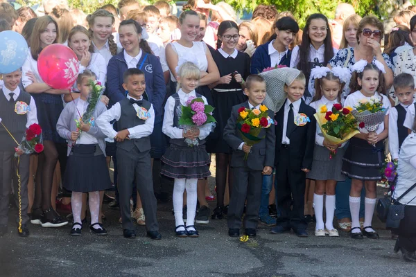 Kinderen met boeketten van bloemen ingeschreven in de eerste klas op school bij de inhuldiging van het schooljaar in de dag van de kennis — Stockfoto