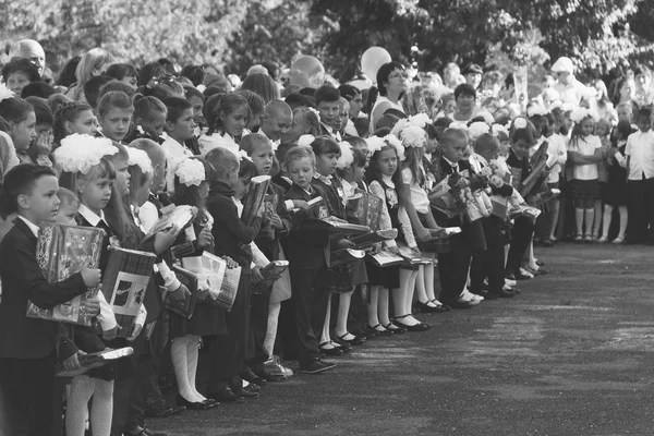 Bambini con mazzi di fiori iscritti in prima classe con insegnanti sulla linea solenne della scuola nel giorno della conoscenza, foto in bianco e nero — Foto Stock