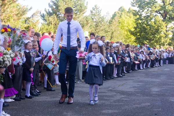 Student, starszych klas i dziewczyna pierwszej równiarka z dzwonkiem w niej ręcznie w szkole uroczyście linijki w dzień wiedzy — Zdjęcie stockowe