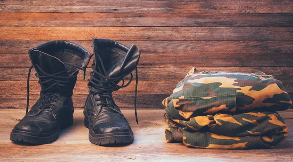 Old leather black men boots and military uniform on a wooden background front view close-up — Stock Photo, Image