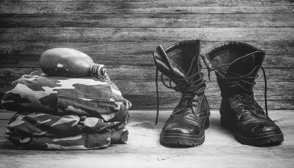 Old leather black mens boots, military uniform and flask for water on a wooden background front view close-up, black and white photo — Stock Photo, Image