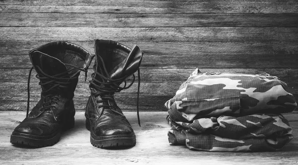Old leather black mens boots ankle boots and a military uniform on wooden background front view closeup black and white photo — Stock Photo, Image
