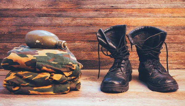 Old leather black men boots ankle boots, military uniforms and a flask of water on wooden background front view closeup — Stock Photo, Image