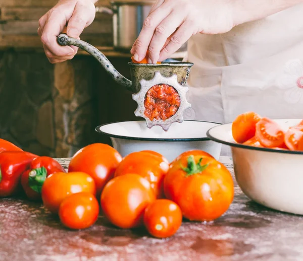 Chef macho retifica pedaços de tomate maduro em um velho moedor manual vintage para fazer molho caseiro, ketchup — Fotografia de Stock