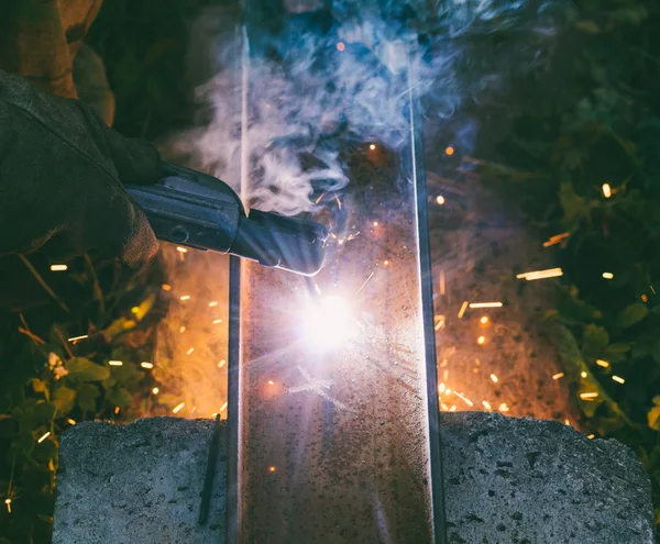 Hombre trabajador soldador quema a través de un agujero de electrodo en un canal de acero por la noche, la vista desde la parte superior — Foto de Stock