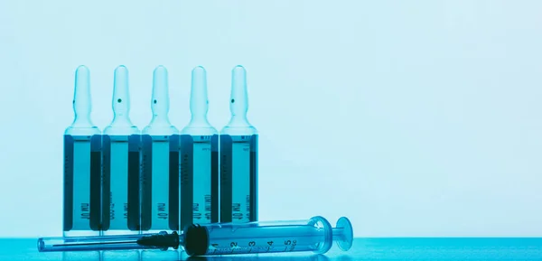 ampoules with a solution for injection and a disposable syringe on a blue background with space for text