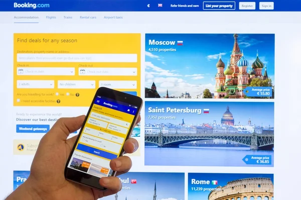 Adıge, Rusya - 16 Ocak 2018: Internet rezervasyon otel baktılar: bilgisayar monitörü erkek elinde Çin Xiaomi smartphone ekranında giriş sayfası