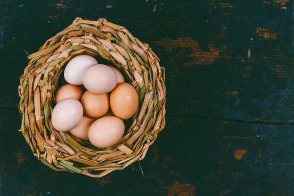 яйца домашних цыплят в плетеной корзине на черном деревянном фоне гранжа с копировальным пространством
