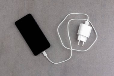Gri arkaplan görünümlü beyaz şarj cihazlı siyah ekranlı akıllı telefon