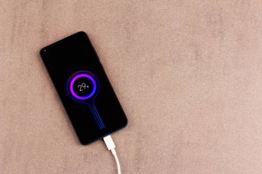 Pembemsi gri arkaplanda beyaz şarj kablosu olan, üzerinde pil göstergesi olan akıllı telefon üst görünümü kapat