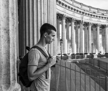 St. Petersburg 'daki Kazan Katedrali' nin sütunlarının yanında duran sırt çantalı ahlaksız bir gencin profil portresi. Siyah beyaz fotoğraf.