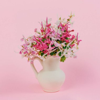 Bir buket pembe, beyaz ve mor kırmızı çiçekle pembe arka planda beyaz bir sürahi içinde hayat.