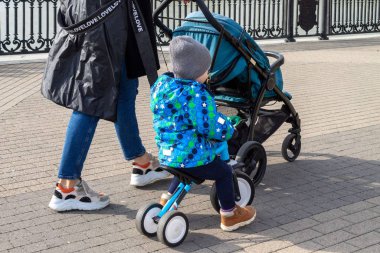 Yavru bir puseti olan genç bir anne ve mekikteki bir çocuk şehir kaldırımında yürüyorlar.