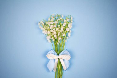 Bir buket mis kokulu çiçekli, mavi arka planda beyaz ve mavi bir fiyonk, üst manzaralı bir vignette.