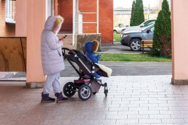 Anne ve çocuk ellerinde akıllı telefonlarla bir bebek arabasında ekranlara, sosyal medya konseptine bakıyorlar.