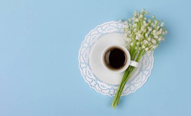 Bir fincan çay tabağında sade kahve ve bir buket nilüfer çiçeği mavi bir arka planda fotokopi alanı, en üstte düz bir manzara