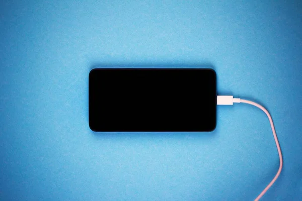 Новый Смартфон Черным Экраном Белым Зарядным Проводом Синем Фоне Вблизи — стоковое фото