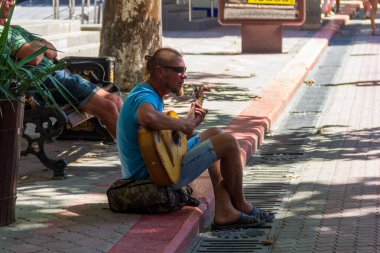 KERCH - 13 Ağustos 2019: Bir sokak müzisyeni yaz günü kaldırımda otururken gitar çalar ve şarkı söyler