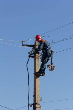 Krasnodar, Rusya - 2 Mart 2020: Bir direğin tepesinde çalışan elektrikçi mavi gökyüzüne karşı yeni elektrik kabloları döşeyecek.