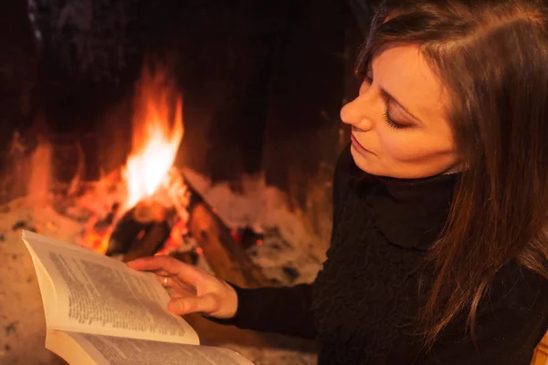 Mulher bonita lendo o livro sentado perto da lareira — Fotografia de Stock