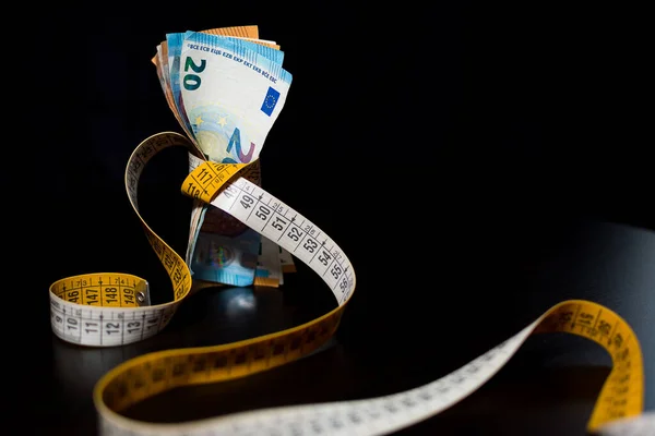 Banknotes tightened by the tape measure on a black background for the concept of financial crisis