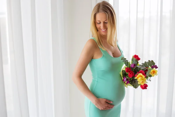 Happy pregnant woman standing with flowers in her hands — Stock Photo, Image