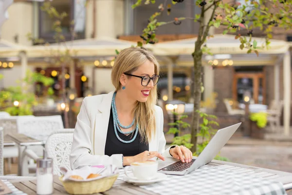 Biznes kobieta siedząc w kawiarni na świeżym powietrzu i pracę na laptopie — Zdjęcie stockowe