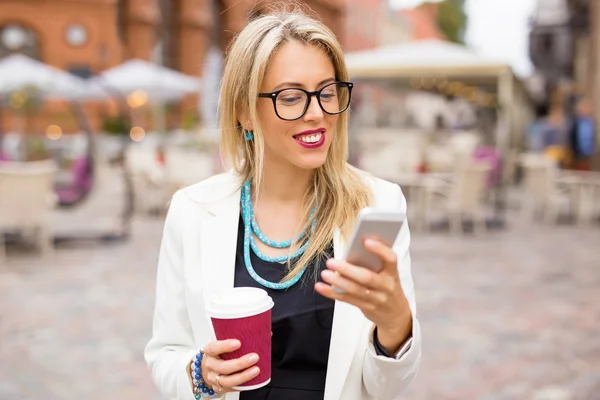 Женщина пьет кофе и пользуется смартфоном — стоковое фото