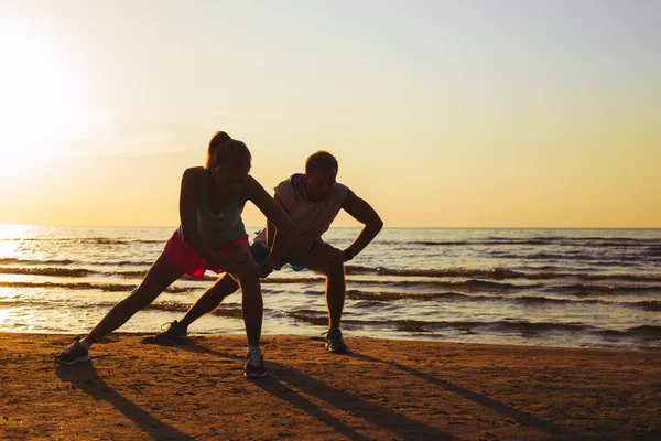 Fitness couple stretching in sunset — Stock Photo, Image