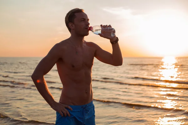 Ajuste o homem bebendo água na praia após o treino — Fotografia de Stock