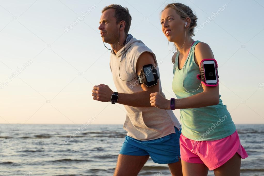 Couple running on the beach during sunset with their headphones plugged in