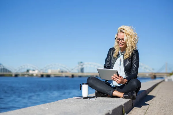Woman sitting by the water and using tablet — Stock Photo, Image