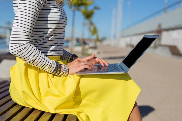 Mujer sentada en el banco afuera y trabajando en la computadora —  Fotos de Stock