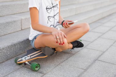Longboard üzerinde otururken Smartphone kullanan kadın