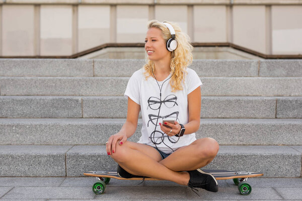 Woman with headphones on her head sitting on longboard