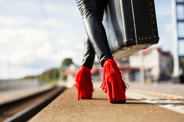 Женщина с красными каблуками и чемоданом на вокзале — стоковое фото