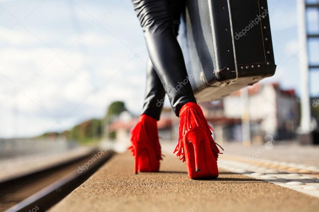 Female with red high heels and suitcase in train station