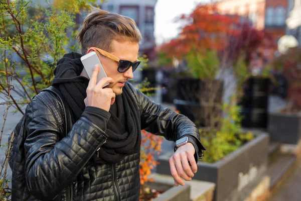 Un uomo elegante che parla al telefono e guarda smartwatch — Foto Stock