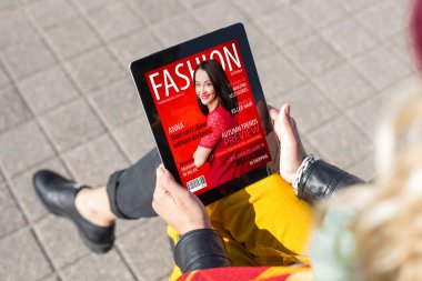 Woman reading fashion magazine on tablet clipart