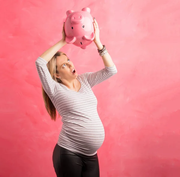 Pregnant woman in shock shaking piggy bank — Stock Photo, Image