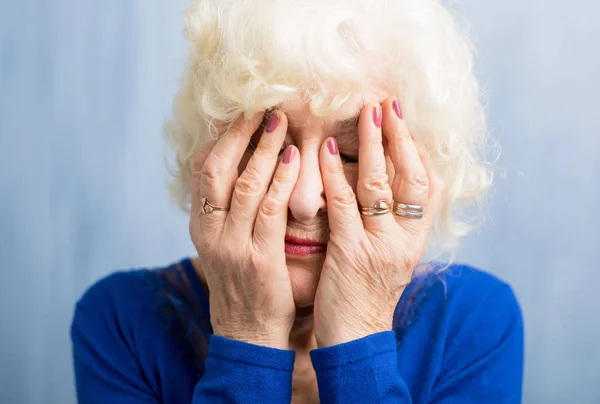 Eldre kvinne dekker ansiktet med begge hender. – stockfoto