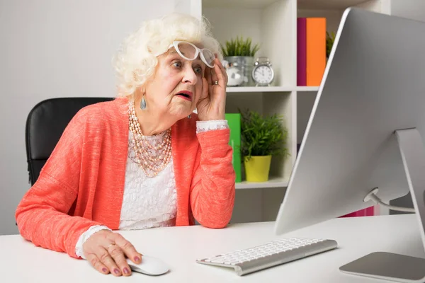 Бабушка работает в офисе и смотрит на компьютер с недоверием — стоковое фото