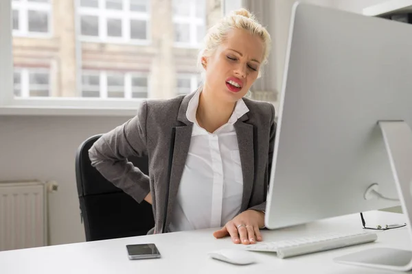 Donna con mal di schiena seduta al computer in ufficio — Foto Stock